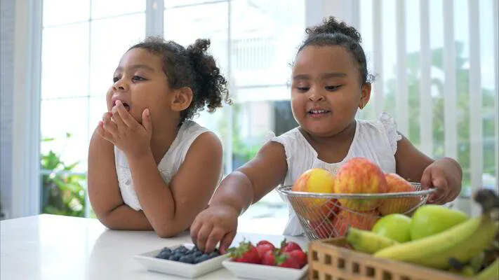 Two girls at a kitchen table with a bowl of fresh fruit and berries