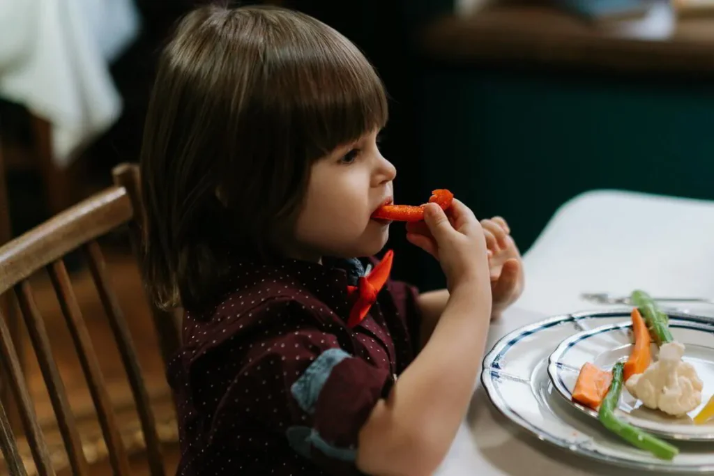 Child eating a slice of red capsicum at the dinner table