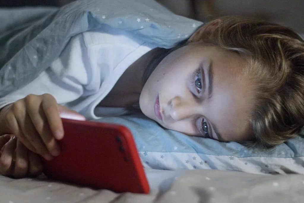Child lying in bed looking at a smartphone screen