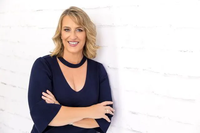Emma Walker standing with her arms crossed against a white brick wall