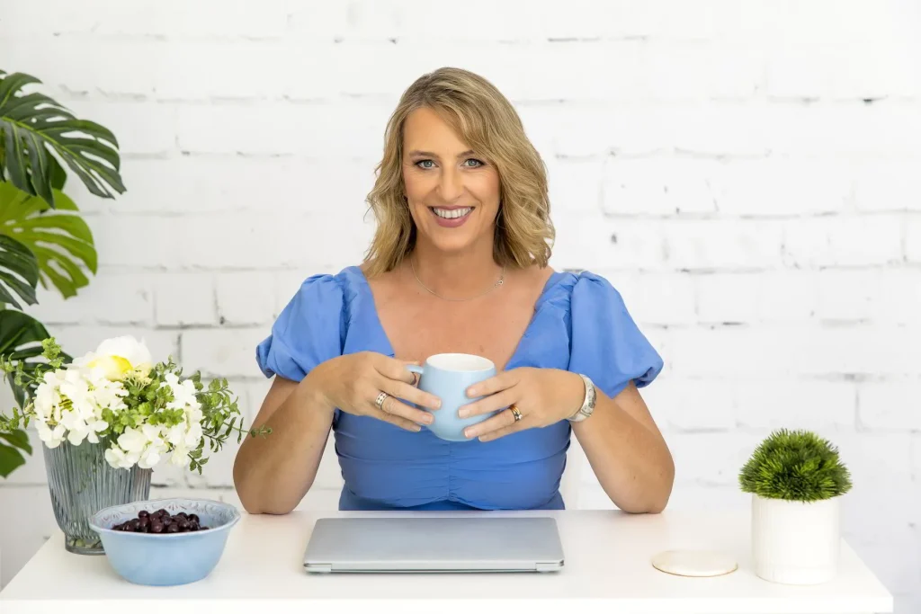 Emma Walker at a white desk holding a cup, with a laptop and a bowl of blueberries