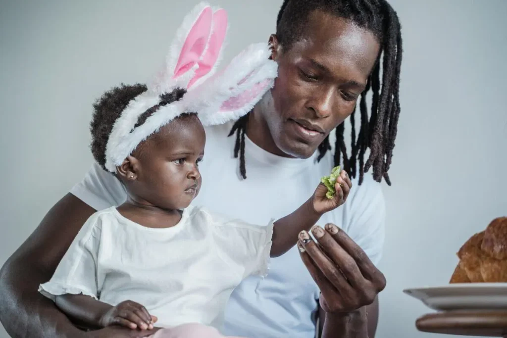 Father helping a toddler in bunny ears eat a snack