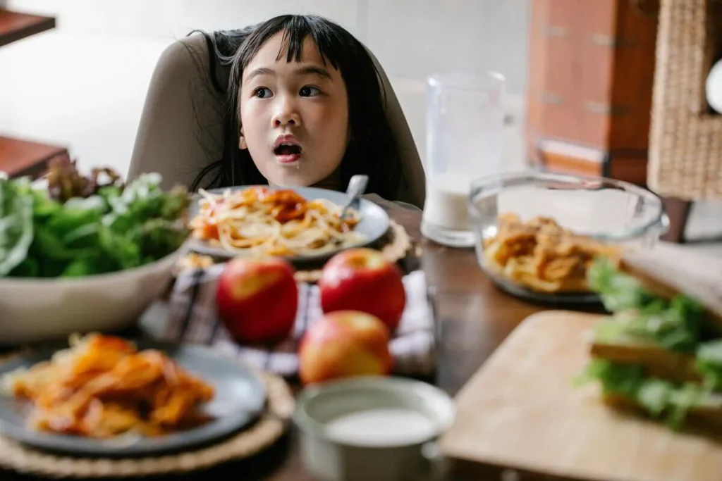 Girl at a table full of healthy dishes including salad, fruit and sandwiches