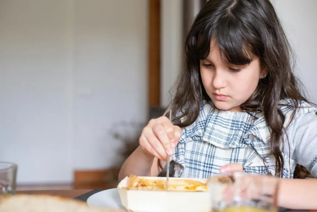 Girl with long hair eating a baked dish at the table