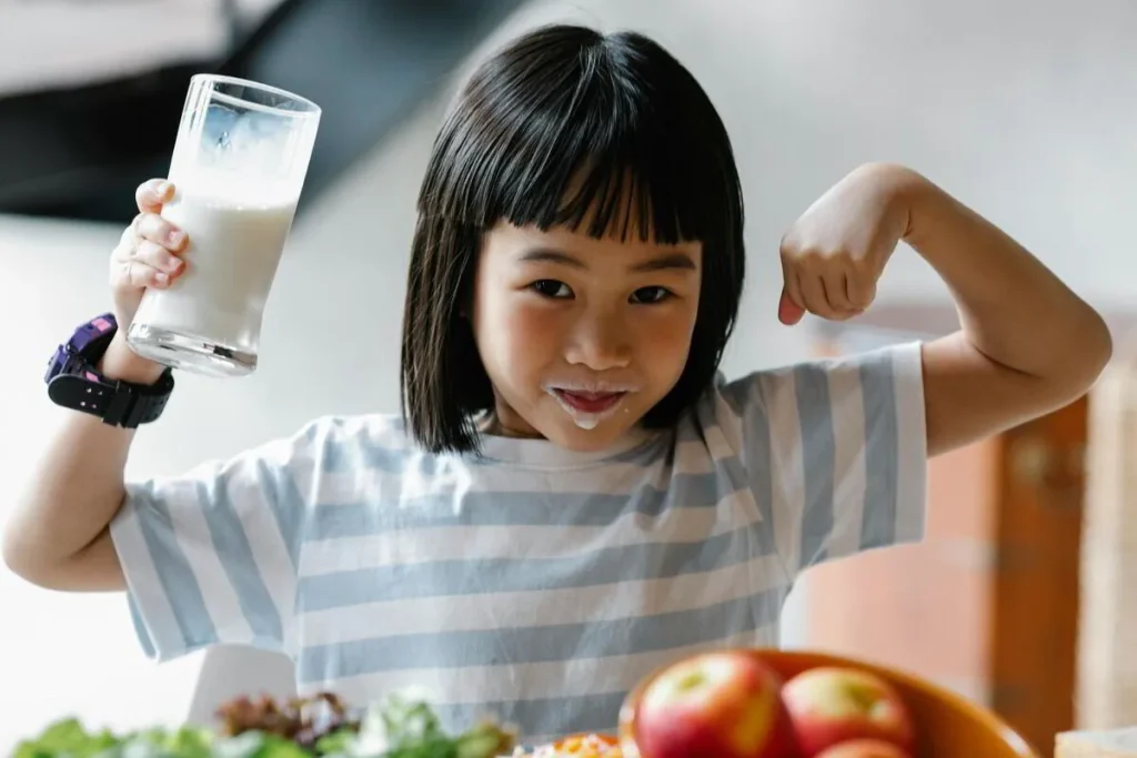 Smiling girl holding a glass of milk and flexing her arm