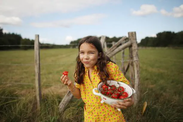 Girl in a yellow dress holding a bowl of strawberries in a field