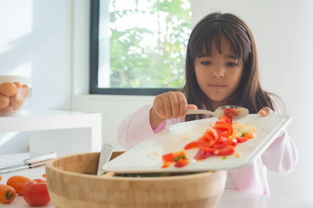 Girl sliding chopped tomato from a board into a bowl