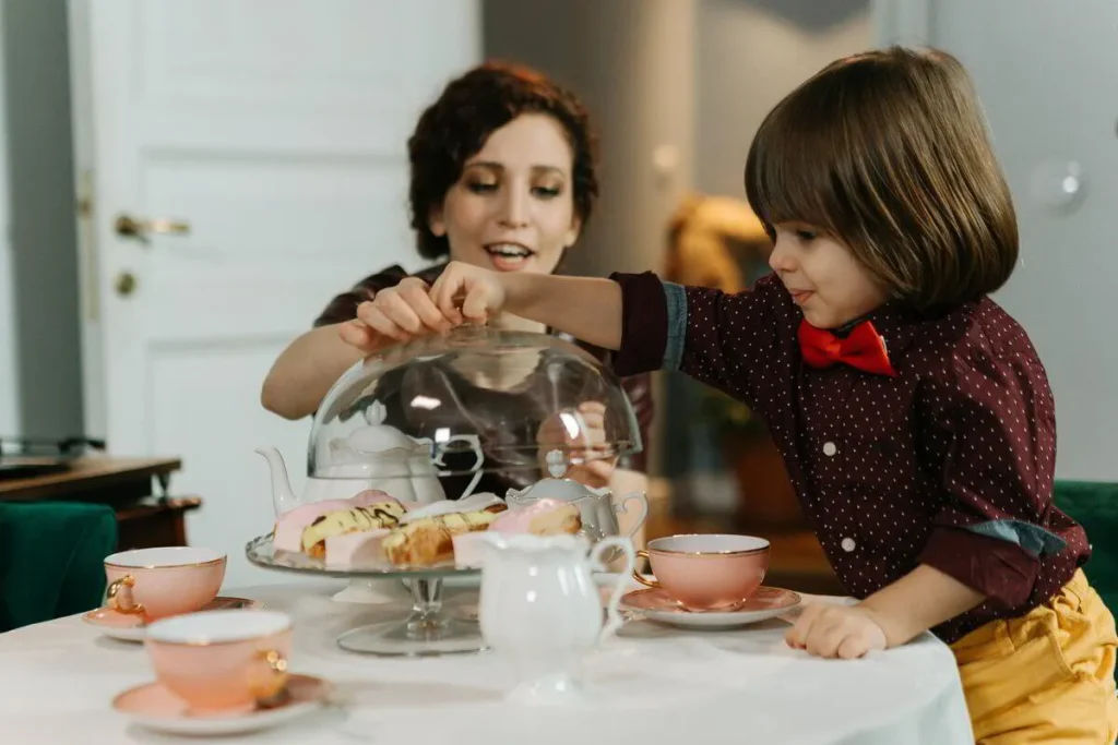 Mother and a young boy in a red bow tie sharing cakes and tea
