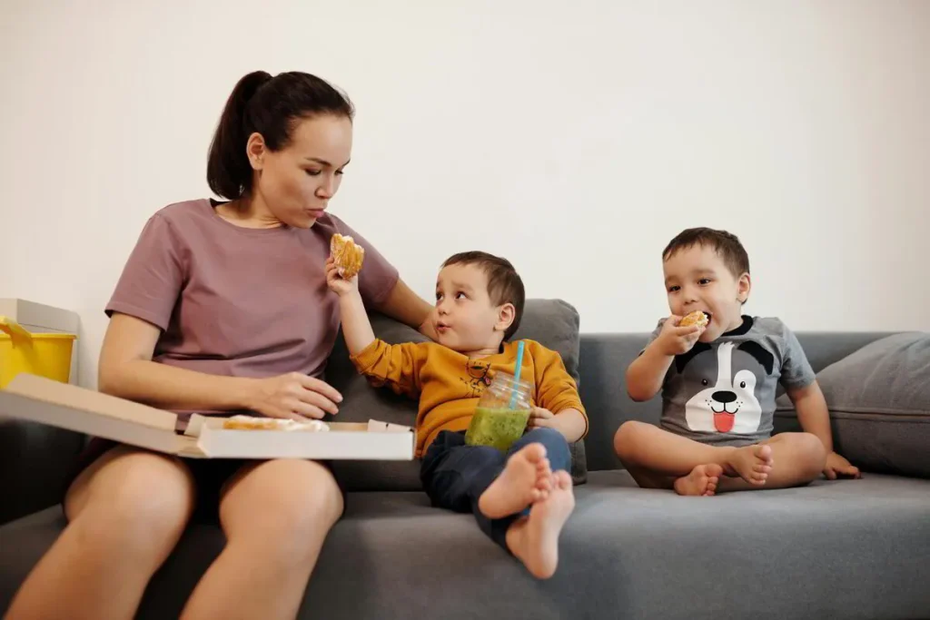 Mother sitting on a sofa with two toddlers having a snack
