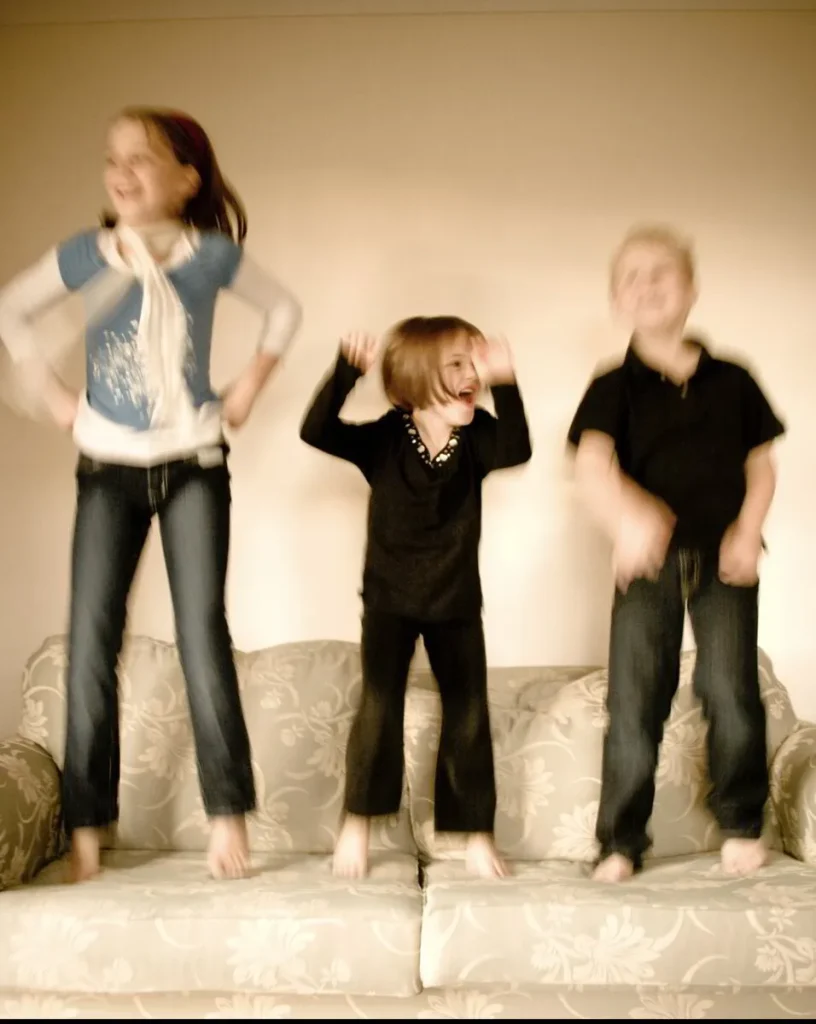 Three children jumping and dancing on a sofa