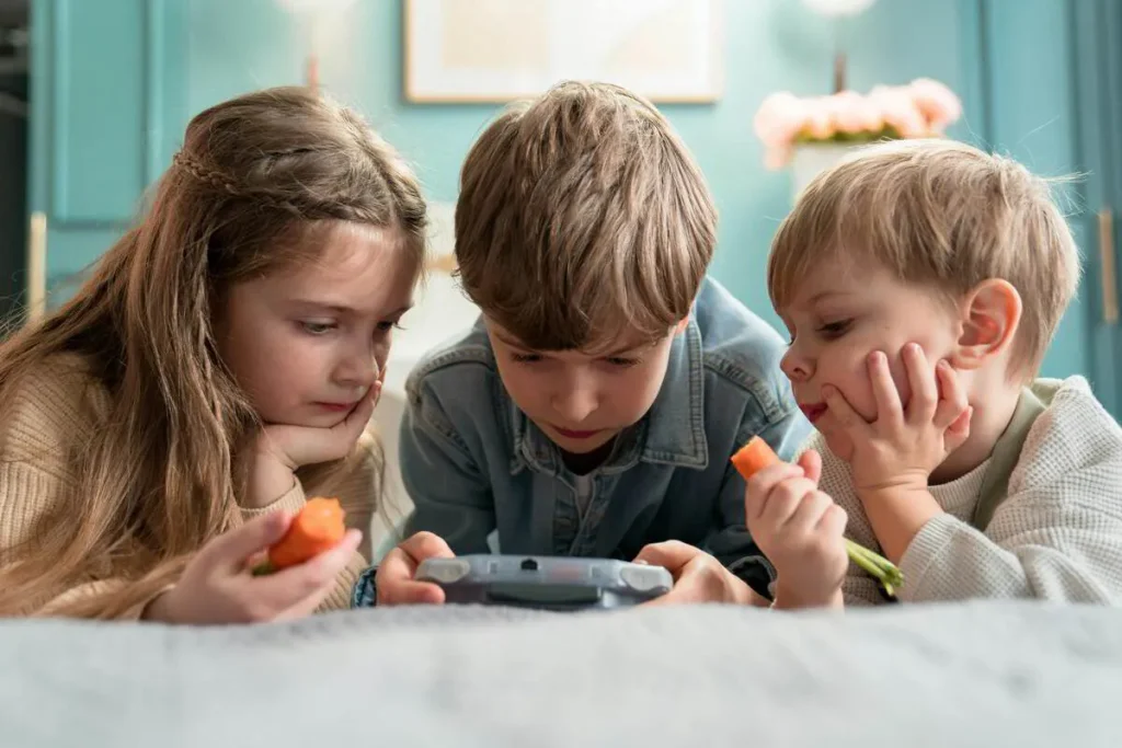 Three children sharing a handheld device on a bed