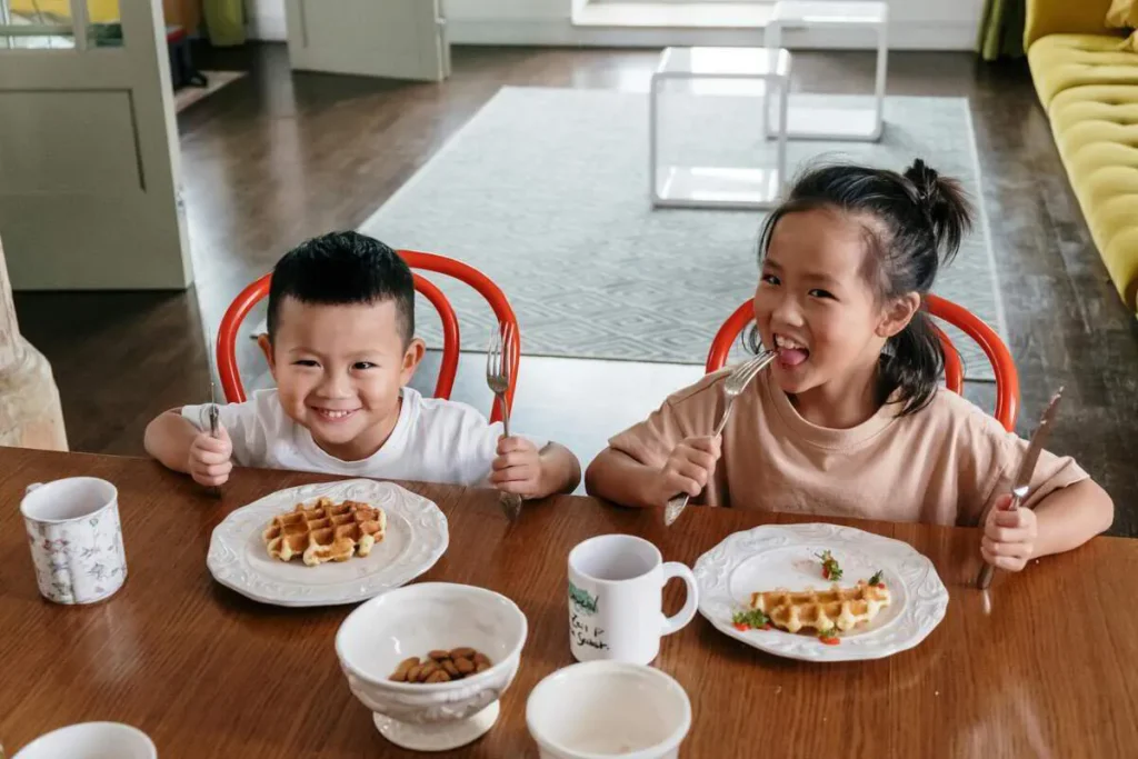 Two smiling children eating waffles at the breakfast table