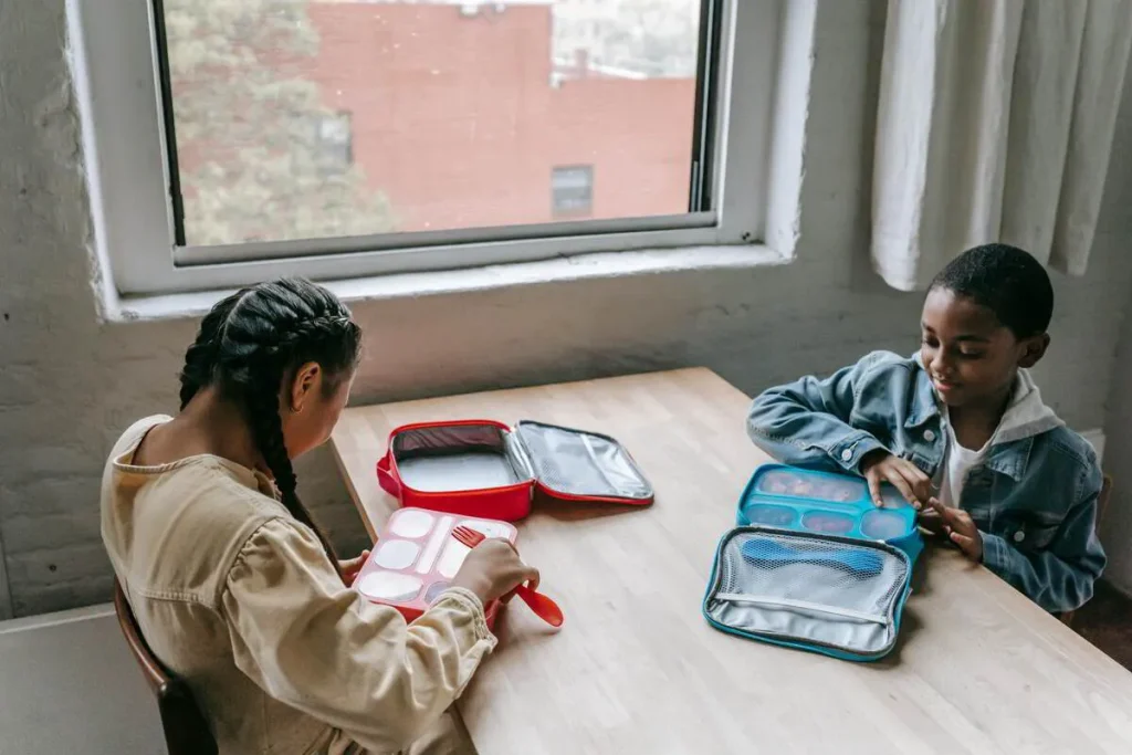 Two children at a table with packed school lunchboxes