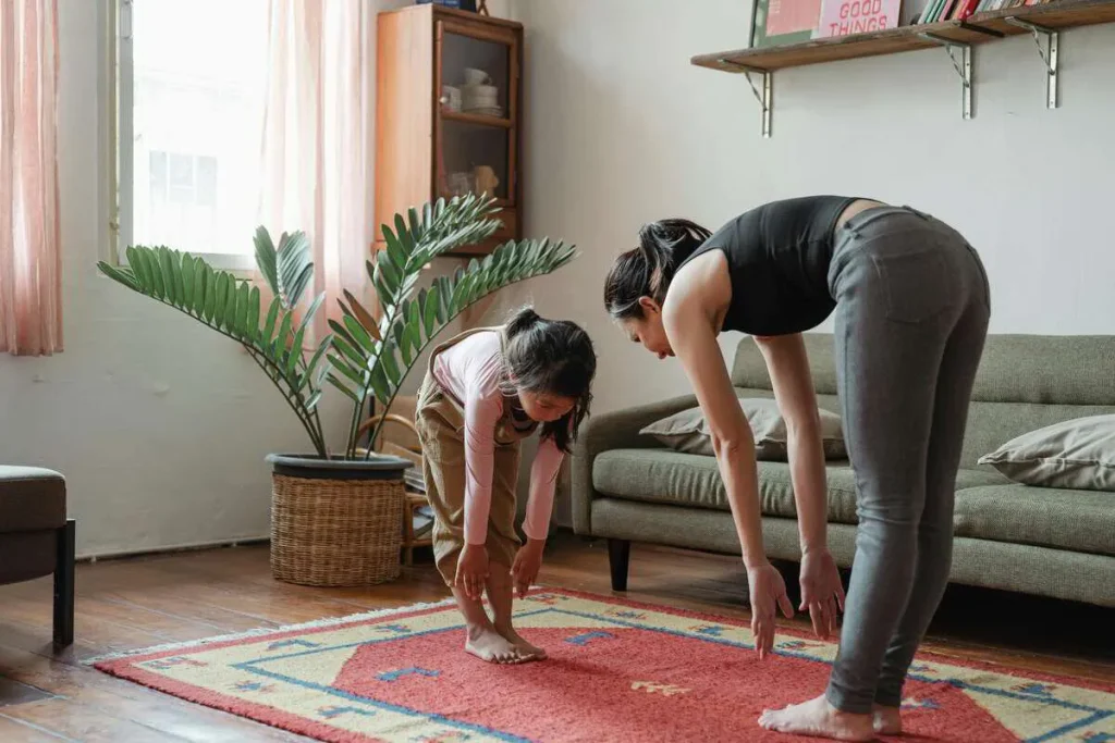 Two people doing a standing forward stretch together in a living room